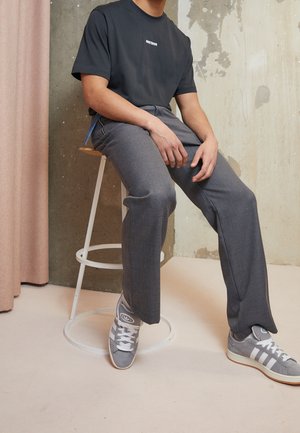 Graue Hosen mit taillierter Passform, kombiniert mit einem schwarzen Kurzarmhemd mit weißem Text. Graue Sneakers runden den Look ab.