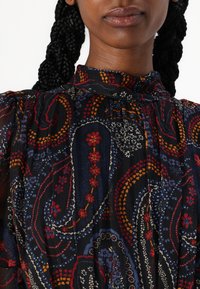 Blusa preta com padrão featuring um colarinho alto, com desenhos florais e paisley multicoloridos, feita de um tecido leve e texturizado.