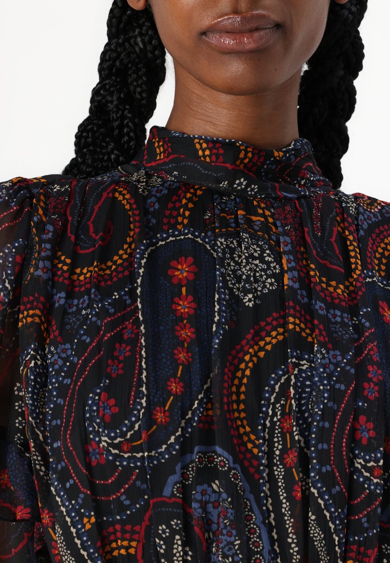 Blusa negra con estampado que presenta un cuello alto, con diseños florales y de paisley en colores variados, hecha de un tejido ligero y texturizado.