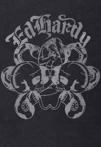 Tela negra con un diseño gráfico gris que presenta serpientes entrelazadas y una figura central. El texto arriba dice "Ed Hardy" en una fuente estilizada.