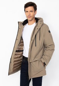 Chaqueta aislante color topo con capucha, cierre de cremallera, múltiples bolsillos y una textura exterior suave. El interior cuenta con un forro acolchado.