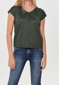 Grön T-shirt med kort ärm och en mjuk, glänsande yta. Enkel design med rundad halsringning, kombinerad med blå jeans.