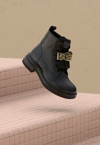 Stivale alla caviglia in pelle nera con suola chunky, fasce con stampa leopardata e fiocchi in glitter nero, che galleggiano sopra gradini rosa piastrellati.