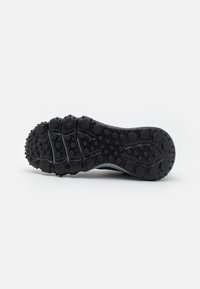Zool van een zwart sportieve schoen met hexagonale en ronde looppatronen, ontworpen voor grip en tractie.
