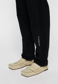 Beige leren loafers met een ronde neus, gedetailleerde stiksel en een brede band. Zwarte spijkerbroek met een geprinte detail aan de zijkant.