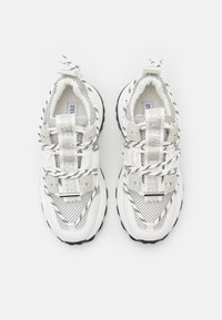 Valged kaetud tennisetossud mustade aktsentidega, paksema tallaga, tekstureeritud mustritega ja silmatorkava rihmaga, millel on kiri "STEVE MADDEN."