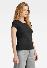 Black cotton t-shirt with a v-neck, short sleeves, and a fitted design. Paired with light gray jeans, showing a casual look.