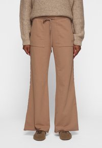 Pantalones de pierna ancha beige, confeccionados en una tela suave, con cintura elástica y dos bolsillos frontales. Textura lisa y ajuste relajado.