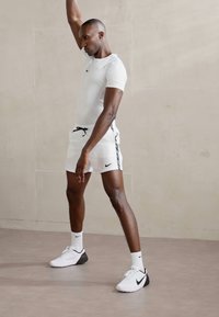 Conjunto deportivo para hombre que incluye una camiseta de manga corta blanca de Nike y pantalones cortos blancos con detalles laterales negros, combinados con zapatillas Nike blancas y negras.