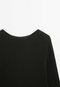 Gros plan d'un pull en tricot noir avec un col rond sur fond blanc.