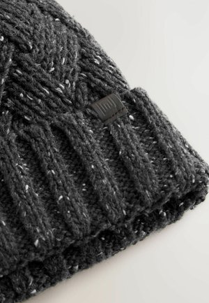 Gebreide grijze beanie met een textuurpatroon en een geribde manchette, voorzien van witte vlekken en een klein zwart leren label.