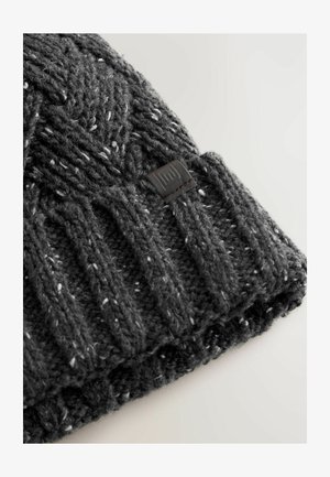 Gebreide grijze beanie met een textuurpatroon en een geribde manchette, voorzien van witte vlekken en een klein zwart leren label.