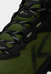 Πράσινο παπούτσι πεζοπορίας με μαύρες λεπτομέρειες, ανώτερο τμήμα από υφασμάτινο πλέγμα με υφή και ανθεκτικό σύστημα κορδονιών. Διαθέτει λογότυπο στη γλώσσα και διακριτικές λεπτομέρειες σχεδίου.