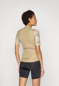 Korte ermer sykkeltrøye i lys beige, med strukturet stoff, slim fit, og en lilla detalj i midjen; kombinert med svarte sykkelskjørt.