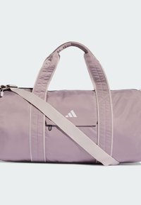 Bolsa deportiva de nailon color púrpura claro con dos asas cortas y una correa larga ajustable. Cuenta con un bolsillo frontal y detalle de logo en blanco.