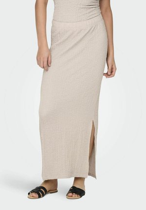 Falda maxi beige texturizada con una abertura lateral, que cuenta con una cinturilla elástica. Combinada con sandalias negras de tiras.