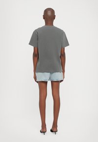 Grå bomull t-skjorte med kortermet, avslappet passform og rund hals. Kombinert med lyseblå denimshorts og svarte høyhælte sko.