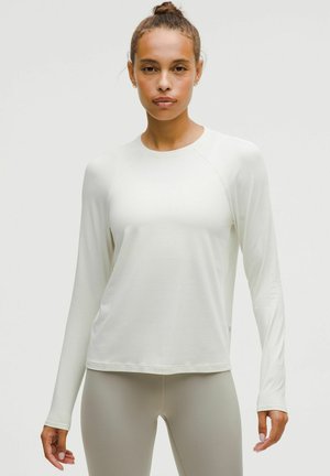 Długi rękaw, jasnobeżowa koszulka sportowa z teksturowanej tkaniny i okrągłym dekoltem, z dopasowanymi rękawami i luźnym krojem u dołu.