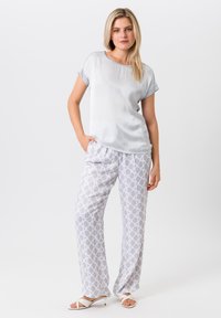 Lichtgrijze satijnen top met opgerolde mouwen, gecombineerd met gestreepte pyjamabroek in grijs en wit met een geometrisch patroon. Witte haksandalen.