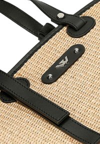 Borsa a rete in paglia intrecciata con manici in pelle nera, dotata di una placca logo in metallo e dettagli hardware argentati. Colore beige naturale e texture liscia.