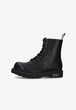 Stivale alla caviglia in pelle nera con punta tonda, chiusura con lacci, suola robusta e linguetta sul retro. Presenta un accento in metallo color argento.