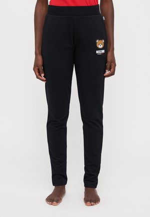 Black jogger pants made of soft fabric, featuring a bear graphic and "MOSCHINO" printed on one leg. Elastic waistband for comfort.