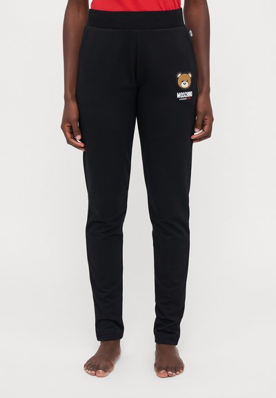 Fekete sportnadrág puha anyagból, medve grafikával és "MOSCHINO" felirattal az egyik lábszáron. Kényelmes gumis derék.