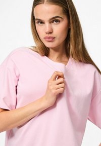 T-shirt in cotone rosa con vestibilità ampia, scollo a V e maniche corte; tessuto liscio senza motivi visibili o dettagli hardware.