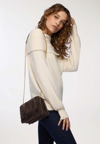 Słomkowy sweter z dzianiny z szerokim ściągaczem na szyi, w połączeniu z ciemną torebką z futra syntetycznego na ramię z złotym łańcuszkiem.