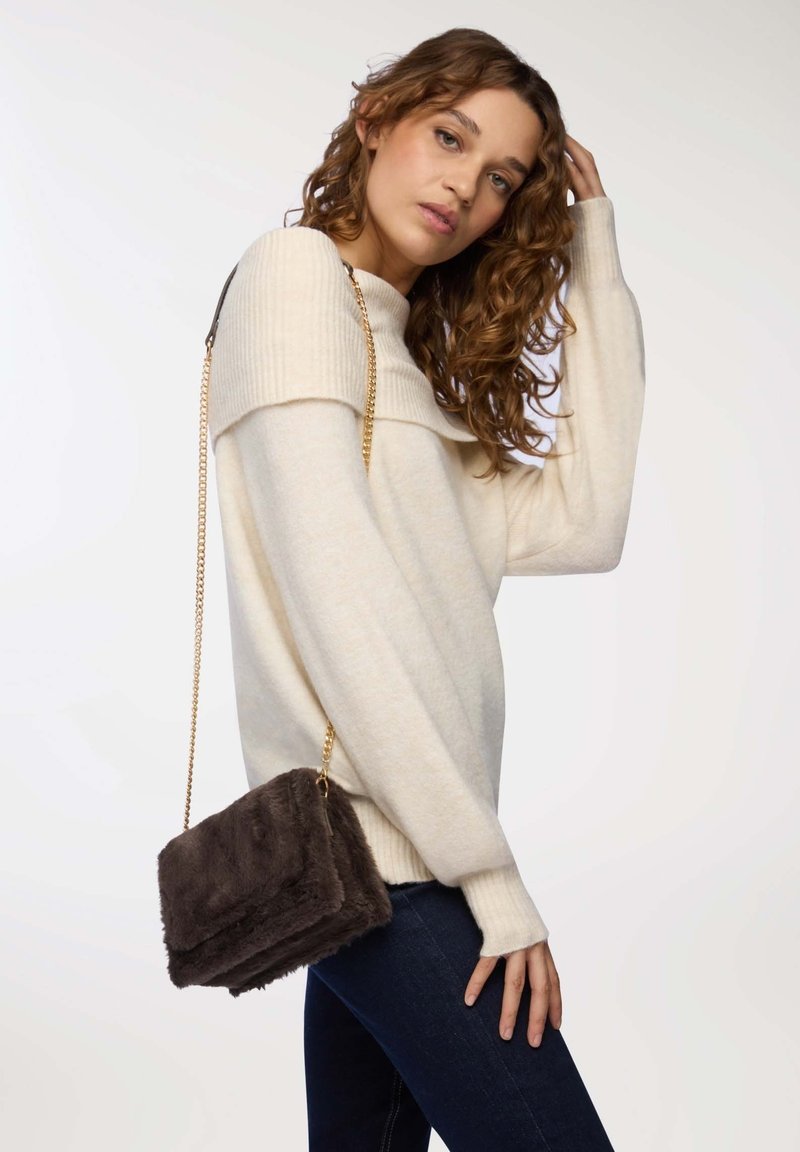 Słomkowy sweter z dzianiny z szerokim ściągaczem na szyi, w połączeniu z ciemną torebką z futra syntetycznego na ramię z złotym łańcuszkiem.