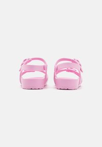 Pink plastic sandals with two adjustable straps and a decorative bow on each side. Textured footbed and patterned sole for grip.