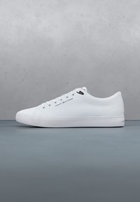 Baskets basses blanches avec lacets blancs, coutures subtiles et petit logo Tommy Hilfiger sur le côté et près de la zone des lacets.