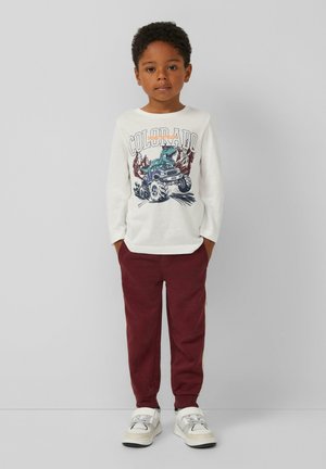 Weißes Langarmshirt mit einem bunten Grafikdruck, der einen Dinosaurier und einen Monstertruck zeigt, kombiniert mit burgunderfarbenen Jogginghosen und hellen Sneakern.