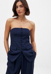 Marineblaues trägerloses Oberteil mit taillierter Passform, Knopfdetail in der Mitte und Seitentaschen. Glattes Material mit strukturierter Silhouette.