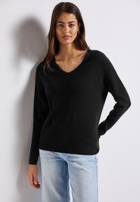 Svart ribbad stickad tröja med V-hals och lång ärm, kombinerad med ljusblå jeans. Slät textur och avslappnad passform.