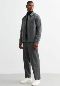 Chaqueta de mezcla de lana gris con un bolsillo en el pecho, combinada con pantalones de patrón a juego y zapatillas blancas, con un diseño de corte recto.