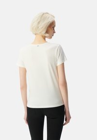 Camiseta blanca de manga corta con cuello redondo y textura suave, mostrada desde atrás, combinada con pantalones ajustados negros.