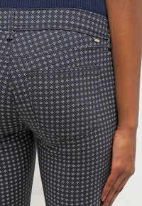 Närbild av en persons nedre rygg och hand som bär marinblå mönstrade byxor med små geometriska former.