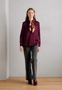Maroon long-sleeve blouse with a collar and button closure, paired with gray flared pants. Brown and peach patterned scarf tied at the neck.