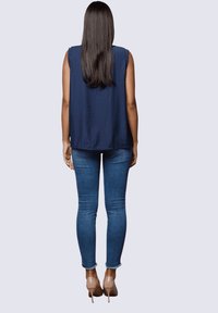 Top de verano sin mangas en color azul marino, con un corte holgado, combinado con unos vaqueros ajustados azules. La modelo lleva unos tacones beige. Textura suave y detalles de diseño sencillos.