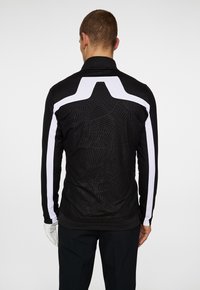 Black long-sleeve shirt with textured pattern and white shoulder accents. Features a high collar and slim fit. Back view displayed.