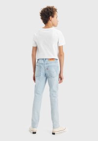 Jeans in denim azzurro chiaro con una vestibilità slim, dotati di una patch in pelle sulla parte posteriore, due tasche posteriori e una finitura leggermente sbiadita. Indossati con una T-shirt bianca.