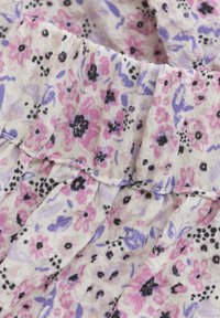 Tissu à motif floral avec de petites fleurs rose, violet et noir sur un fond crème. La texture est douce et légèrement froissée.
