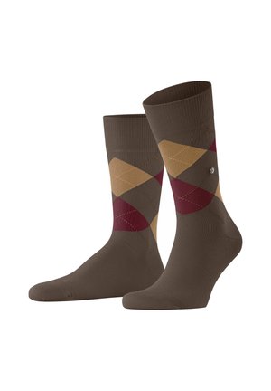 Une paire de chaussettes marron mi-mollet avec un motif argyle en diamants dans les tons beige, bordeaux et marron foncé, et un petit épinglette en métal sur le côté.