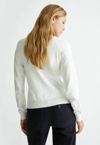 Maglione bianco lavorato a maglia con polsini e orlo a coste, mostrato da dietro, abbinato a jeans scuri. Texture liscia, vestibilità casual.