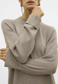 Beige gestrickter Pullover mit Rippstruktur und weiten Ärmeln, ausgestattet mit einem Rundhalsausschnitt und subtilen Nahtdetails an den Schultern.