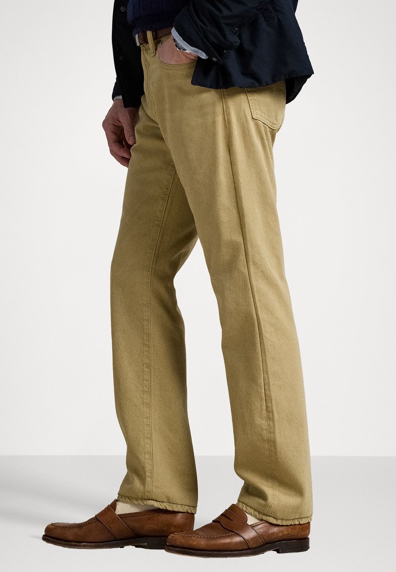 Beige Baumwollhosen mit geradem Schnitt, ausgestattet mit einer feinen Textur und Seitentaschen, kombiniert mit braunen Lederschuhen.