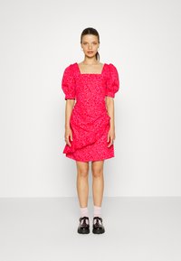 Vestido floral rosa com decote quadrado, mangas bufantes e bainha em camadas. Usado com sapatos de plataforma pretos e meias rosas.