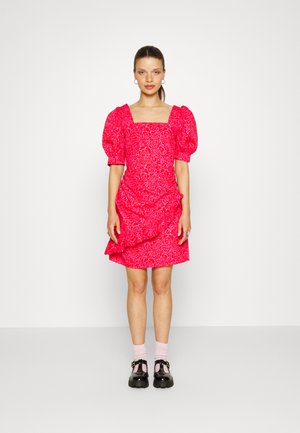 Vestido floral rosa com decote quadrado, mangas bufantes e bainha em camadas. Usado com sapatos de plataforma pretos e meias rosas.