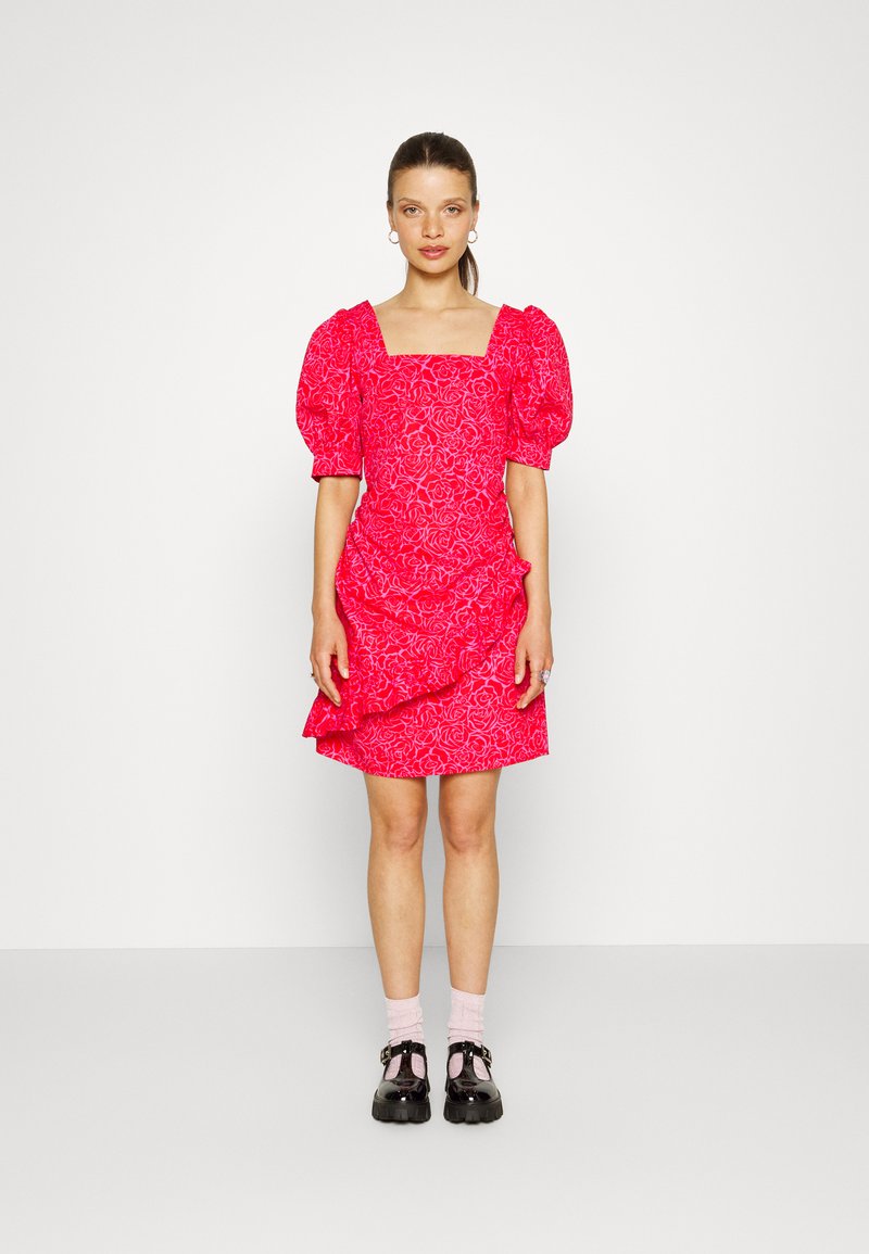 Vestido floral rosa com decote quadrado, mangas bufantes e bainha em camadas. Usado com sapatos de plataforma pretos e meias rosas.